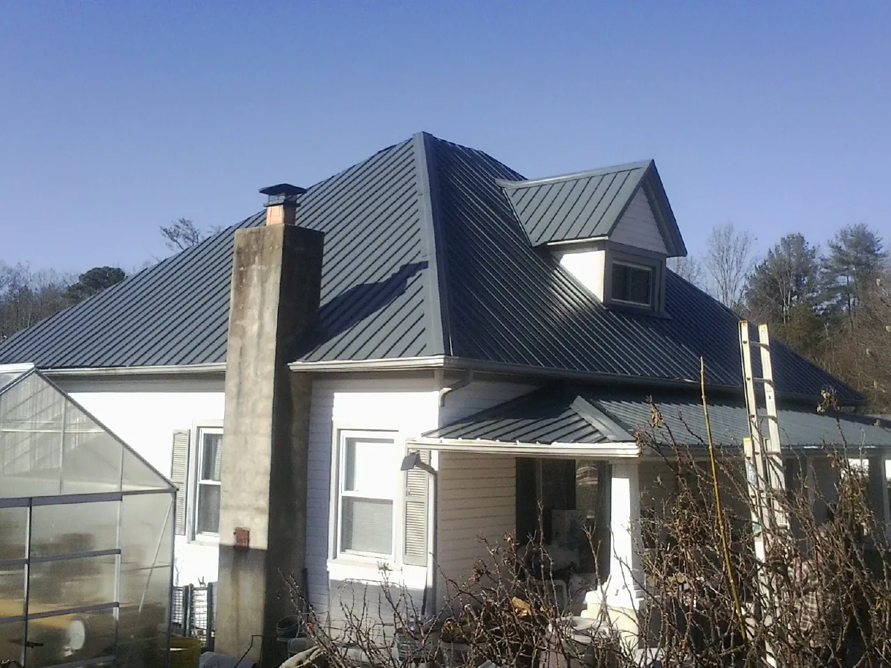 Dark blue standing seam metal roof on a white farmhouse with dormer — Slate & Tile Roof Repair by Roofing Brothers in Whitmore Lake