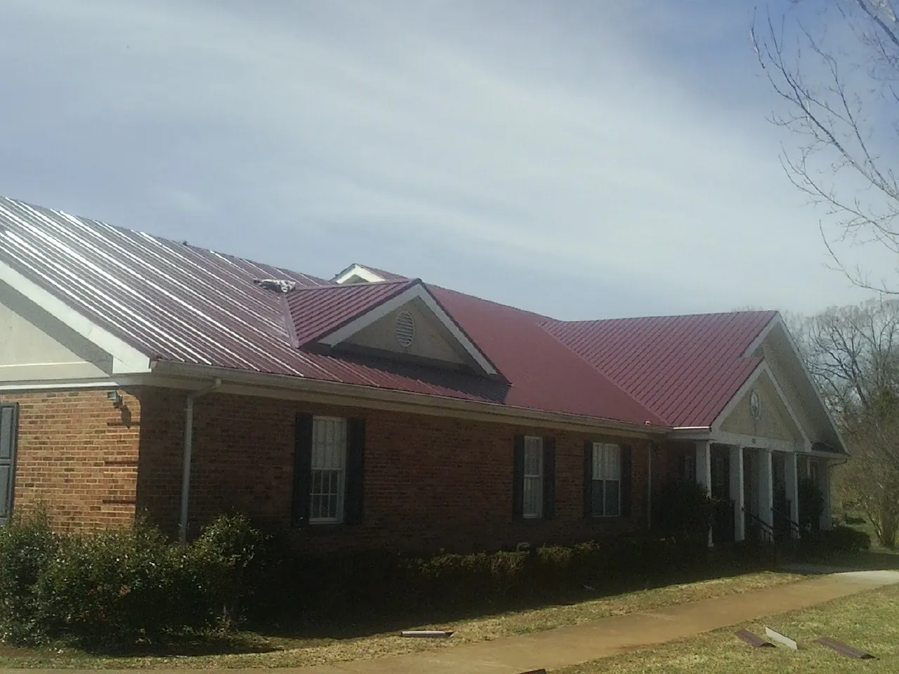 Red metal roof with gabled entries on a long brick building, from a Hail Damage Roof Repair job in Whitmore Lake