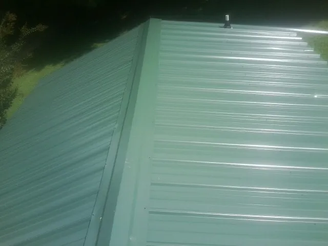 New green metal panels meeting at the ridge of a roof — Flat Roof Repair work by our crew in Whitmore Lake