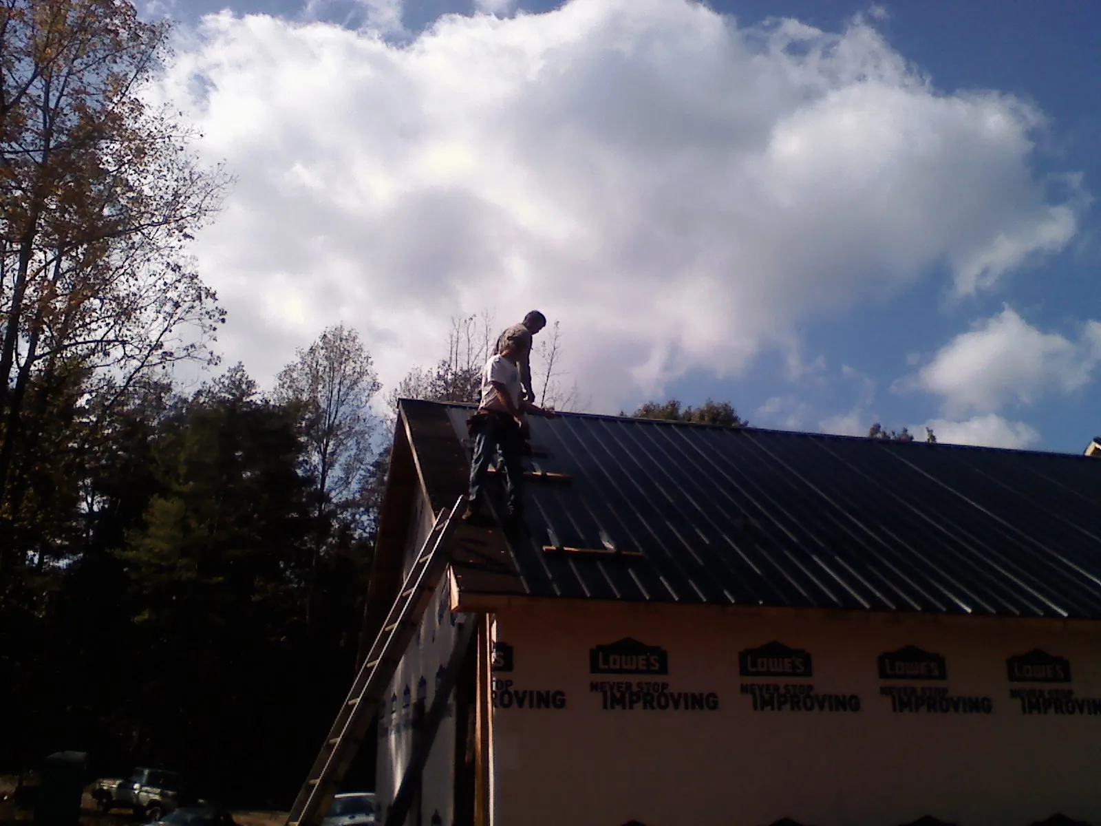 Roofer fastening dark metal panels high against a cloudy sky, from a Roof Inspection job in Whitmore Lake