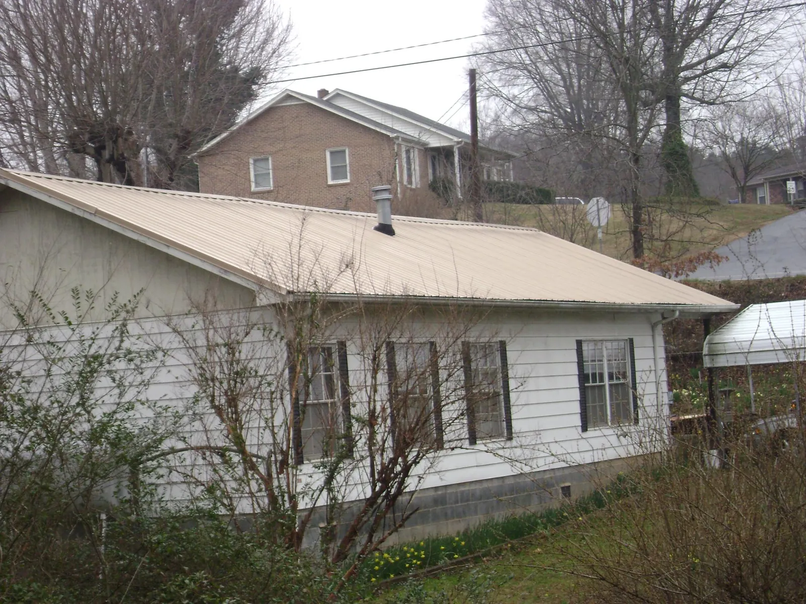 Tan metal roof on a white sided house set into a hillside — Commercial Roofing by Roofing Brothers in Whitmore Lake