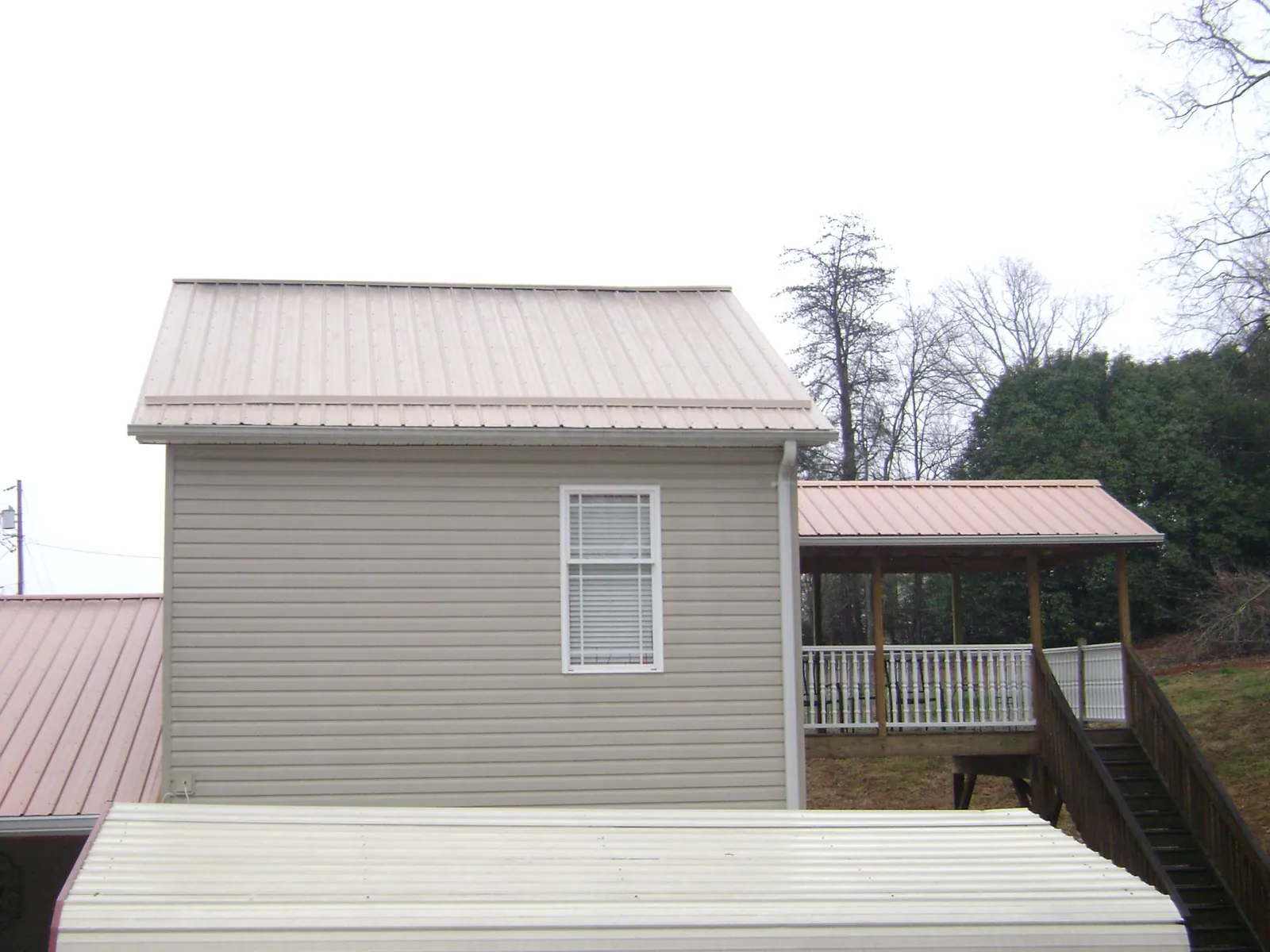 Tan metal roofs on a two story addition and attached porch, from a Roof Replacement job in Whitmore Lake