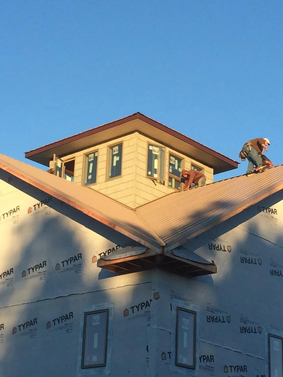 Roofers working around a rooftop cupola on a new metal roof at sunset — Roof Waterproofing in Whitmore Lake by Roofing Brothers